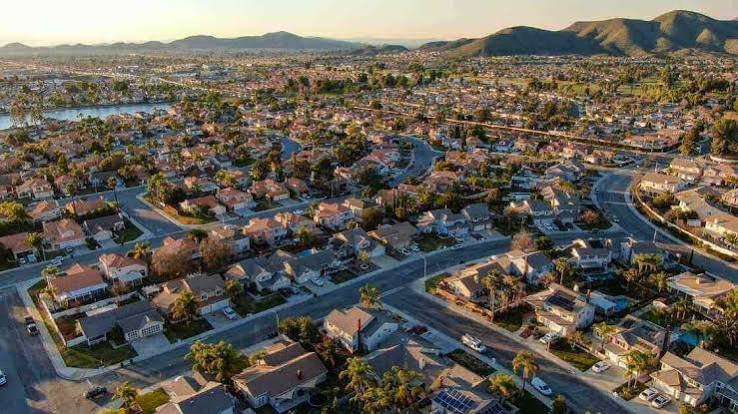 Aerial view of a French Valley neighborhood at golden hour, with rows of homes, a small lake, and mountains beyond