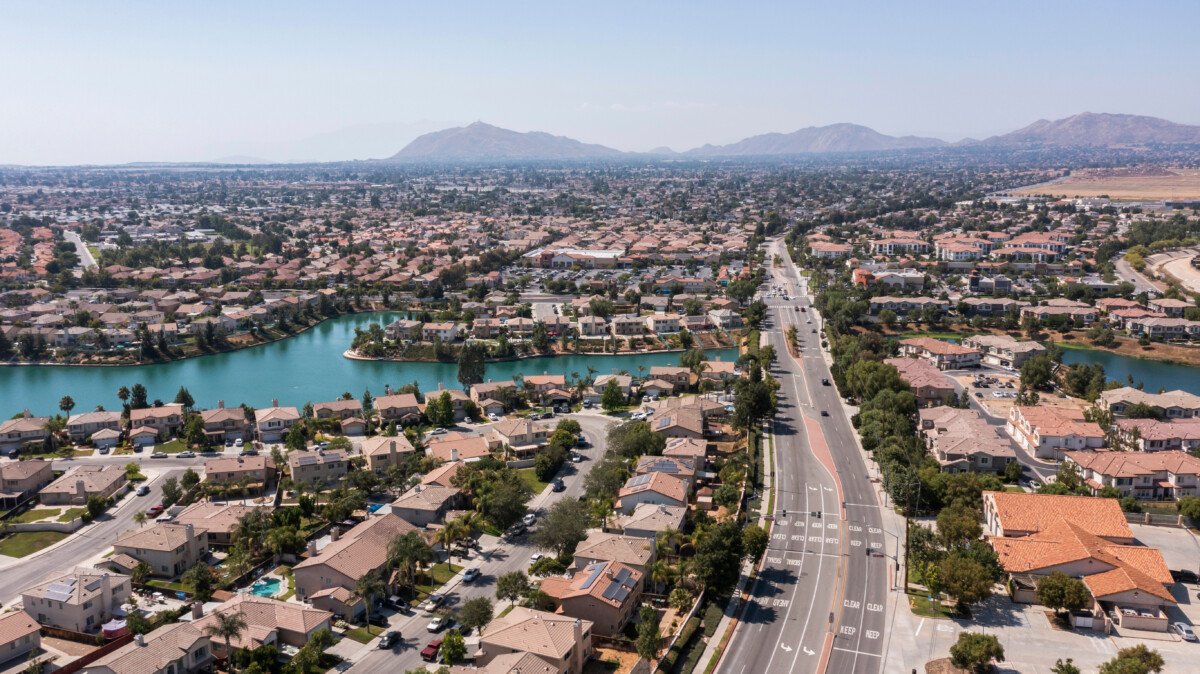 Aerial view of a Moreno Valley neighborhood with homes lining a blue lake and Box Springs Mountain in the distance