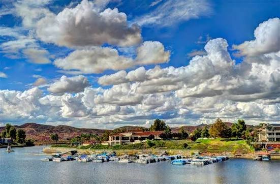 A wide view of Canyon Lake with boats moored at the docks, lakeside homes, and dramatic clouds overhead