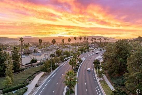 A palm-lined Corona boulevard winding through neighborhoods at sunset, with the Santa Ana Mountains in the distance