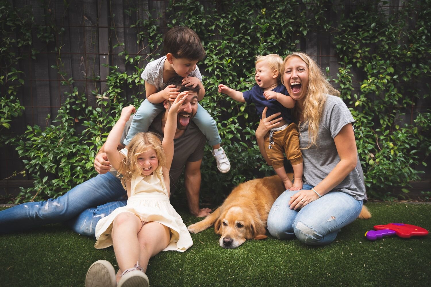 A happy French Valley family with two young children and their golden retriever laughing together on the backyard lawn
