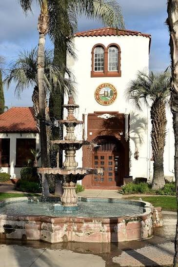 Historic Spanish-style landmark with a fountain and palm trees in downtown Perris