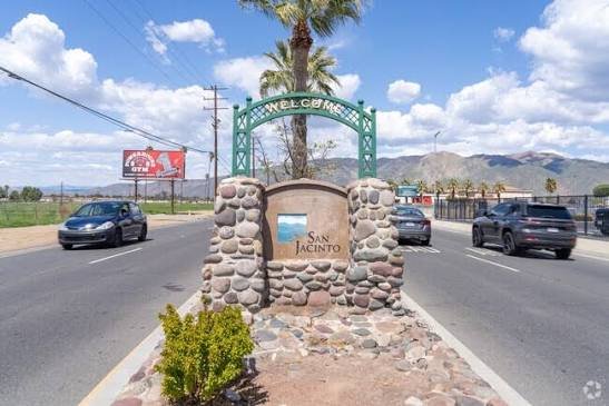 The stone Welcome to San Jacinto sign along the roadway, with the San Jacinto Mountains rising behind it