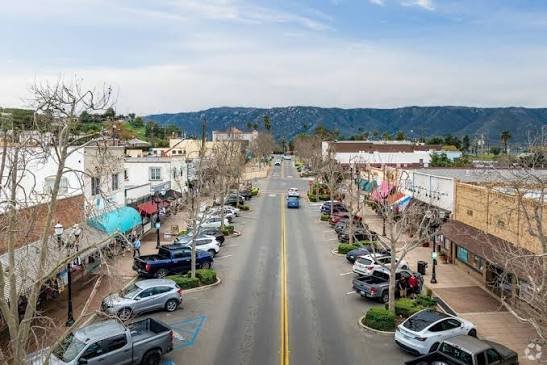 Aerial view down historic Main Street in Lake Elsinore, with storefronts, parked cars, and the Ortega Mountains beyond