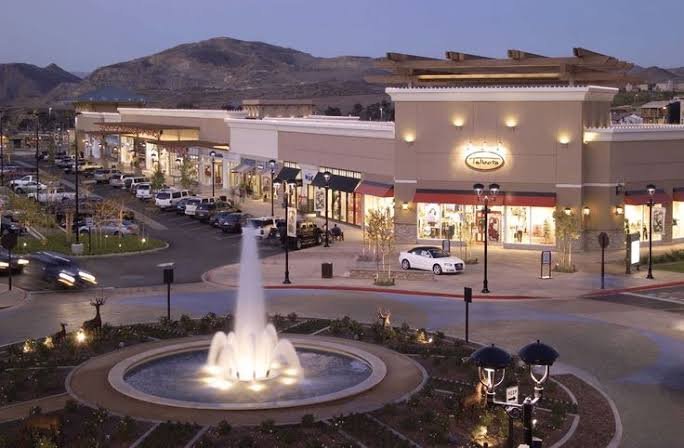 An illuminated fountain in a Corona shopping center plaza with the hills behind at dusk